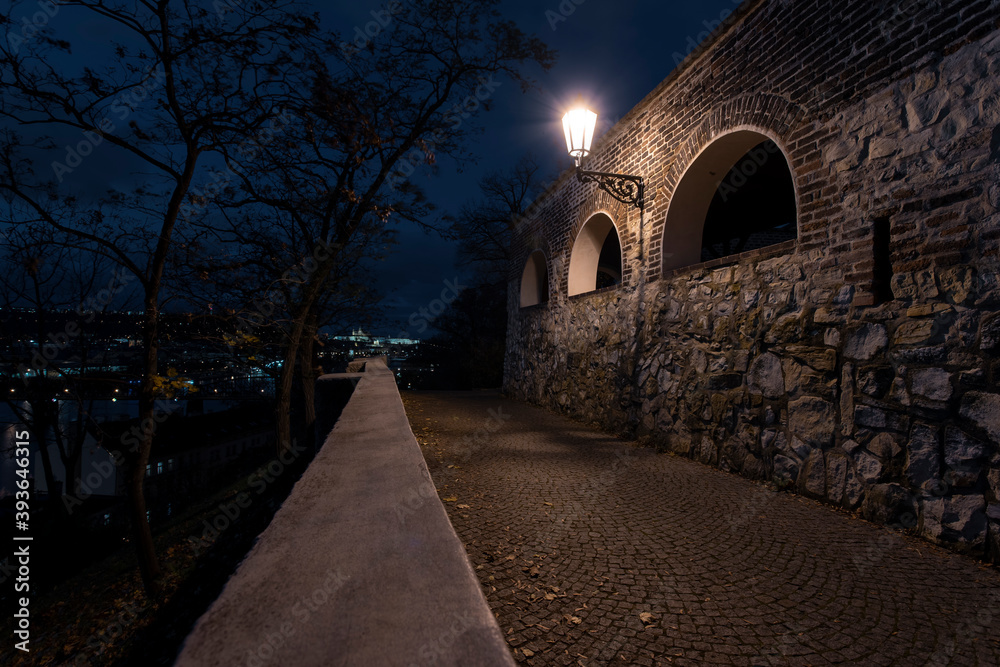 Obraz premium light from street lighting and old stone fortress walls from the 15th century and paving blocks on the ground for pedestrians at night in the center of prague in the czech republic and in the backgro