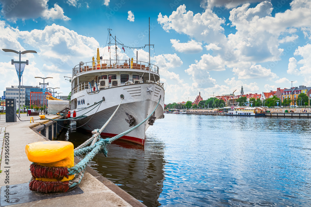 Fototapeta premium Large boat docked or moored on Customs Quay, view on promenade and boulevards on Odra River embarkment with old town in background in Szczecin, Poland