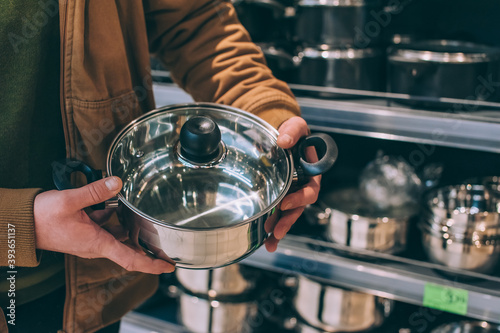 A man in a supermarket holds a metal pot with a lid.