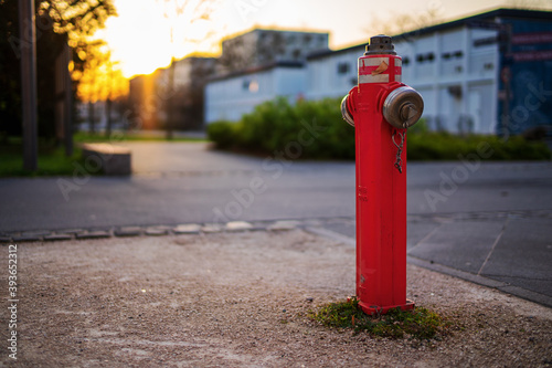 Red water hydrant on the street in the evening with the sunset in the background