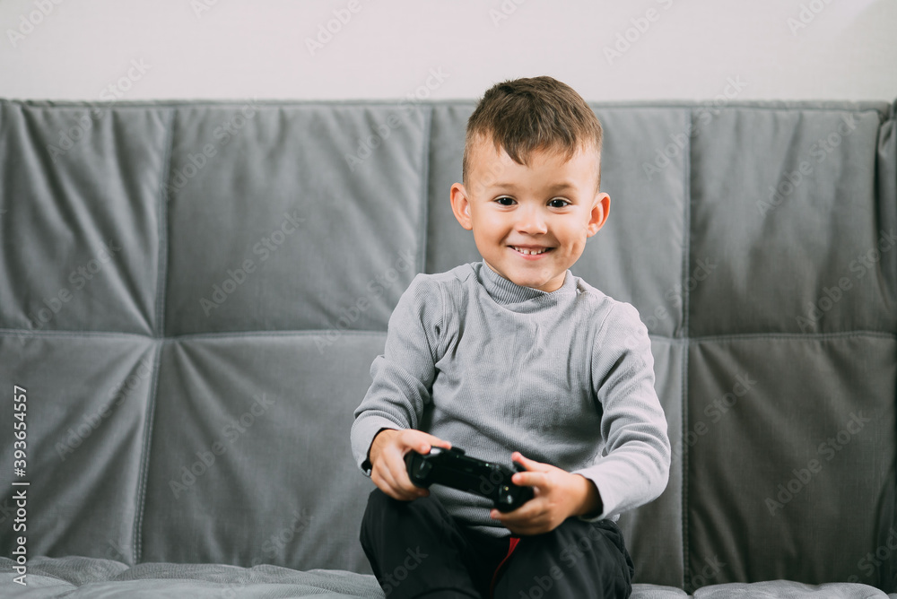 A little boy playing a video game while sitting on the couch reacts emotionally A little boy playing a video game while sitting on the couch reacts emotionally