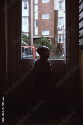 The girl out of focus looks out the window that opens onto the courtyard of a high-rise building. Drama background with kid