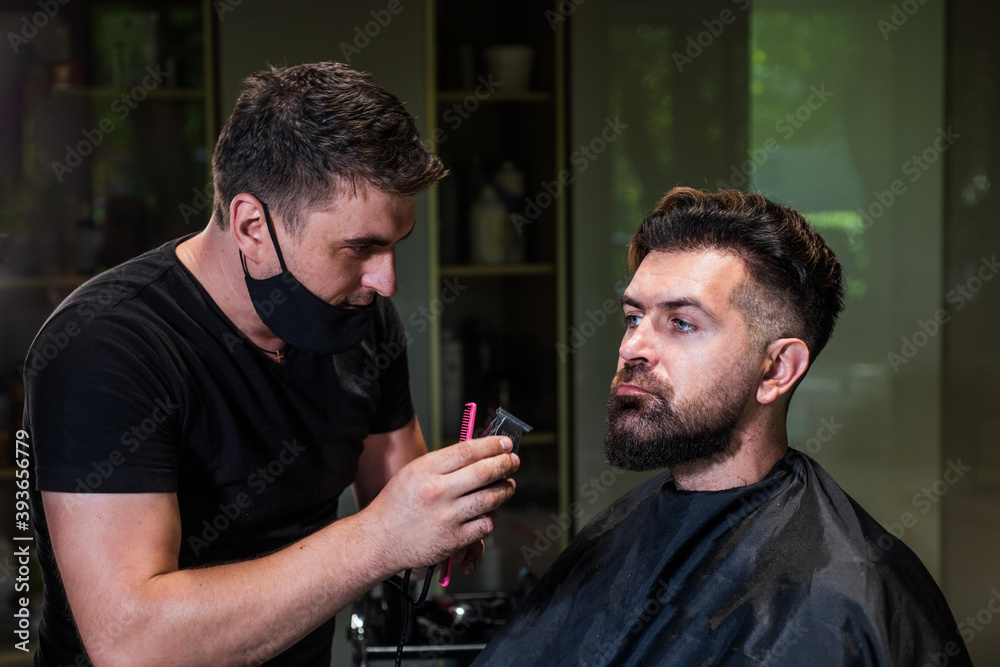 attractive barber making haircut of handsome guy in barbershop, hairdressing tools