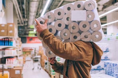A shopper in a supermarket holds a package of toilet paper.