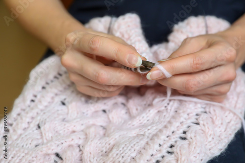 Woman's hand holding needles and knitting pink clothing detail