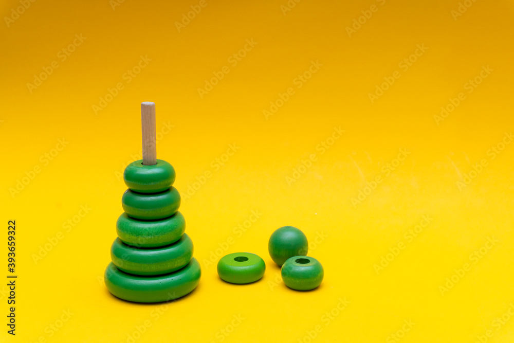 Pyramid build from green children wooden toy rings at yellow background, toy for baby and toddlers. Child development concept. Pyramid build from green children wooden toy rings at yellow background, toy for baby and toddlers. Child development concept.