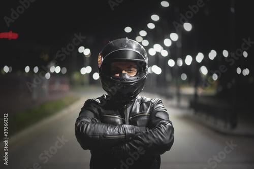 Fototapeta Naklejka Na Ścianę i Meble -  Motor biker in a helmet with open visor is standing on the night road.
