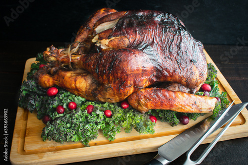 Roast Turkey on a Carving Board: A whole turkey on a bamboo carving board garnished with kale and cranberries