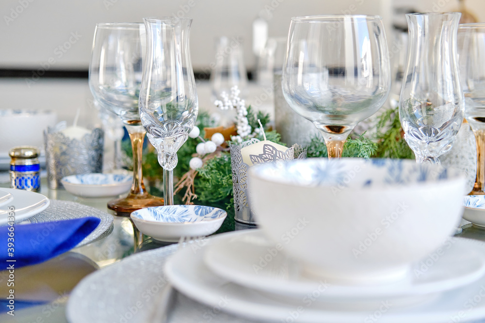 Christmas dinner and New Year celebration concept. Close up view white dishware blue napkins decoration on the table ready for quest reception, ornate table setting with candle and xmas wreath