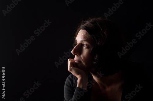 Profile portrait of serious woman with hand on chin and thinking on black background