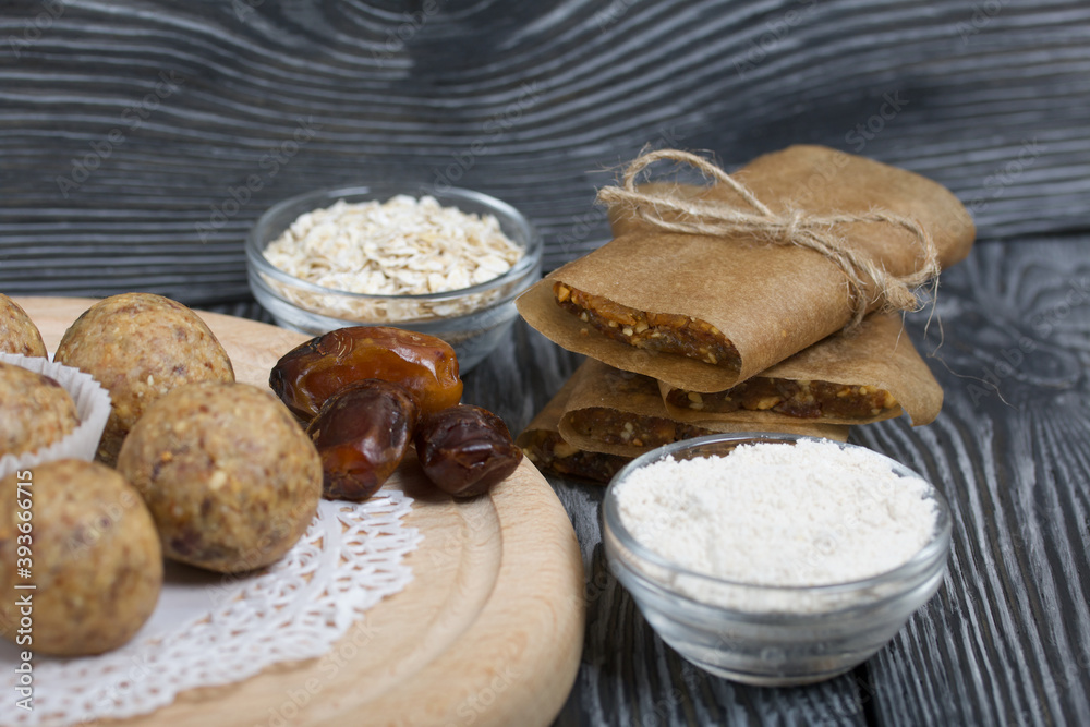Fototapeta premium Dried fruit and oatmeal sweets. Nearby ingredients for their preparation. On black pine boards.