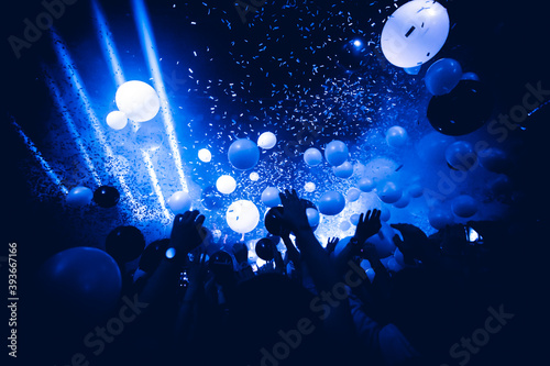 Rave party. Silhouettes of concert crowd in front of bright stage lights and confetti. 