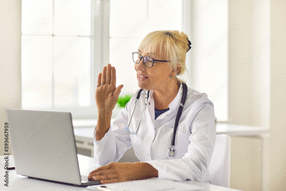 Side view friendly senior female doctor greets the patient and conducts an online consultation. Side view friendly senior female doctor greets the patient and conducts an online consultation.