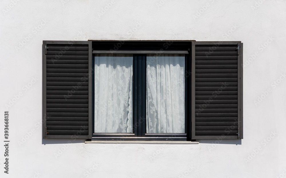 Wooden window with black shutters on a white facade