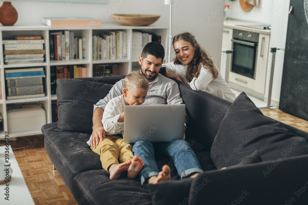 happy young family sitting on sofa and using laptop computer at home happy young family sitting on sofa and using laptop computer at home