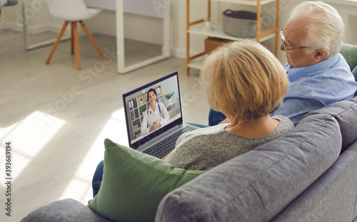 Quadro su tela Senior couple sitting on couch with laptop and having video call with online doc