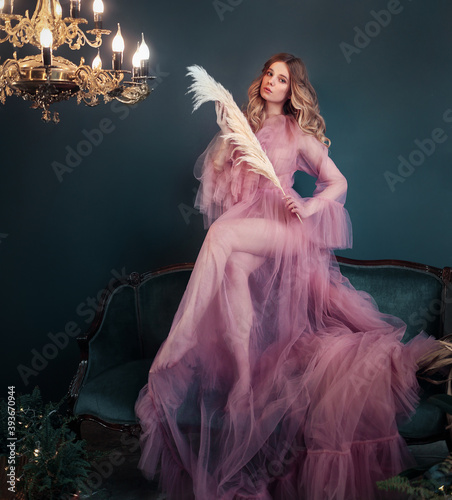 Beautiful young woman in pink transparent dress with feather in hands