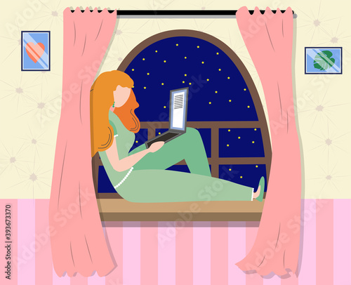 A woman works at a laptop while sitting on the windowsill at home. Freelance concept, quarantine due to covid-19