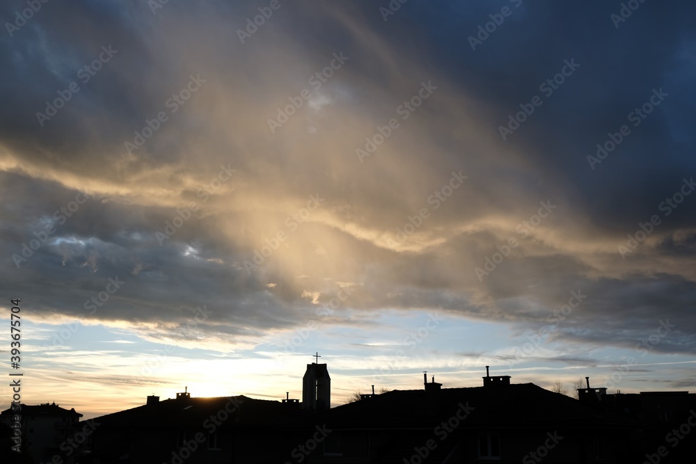 Beautiful cityscape with dark silhouette of town on horizon and colorful clouds with light during sunrise.