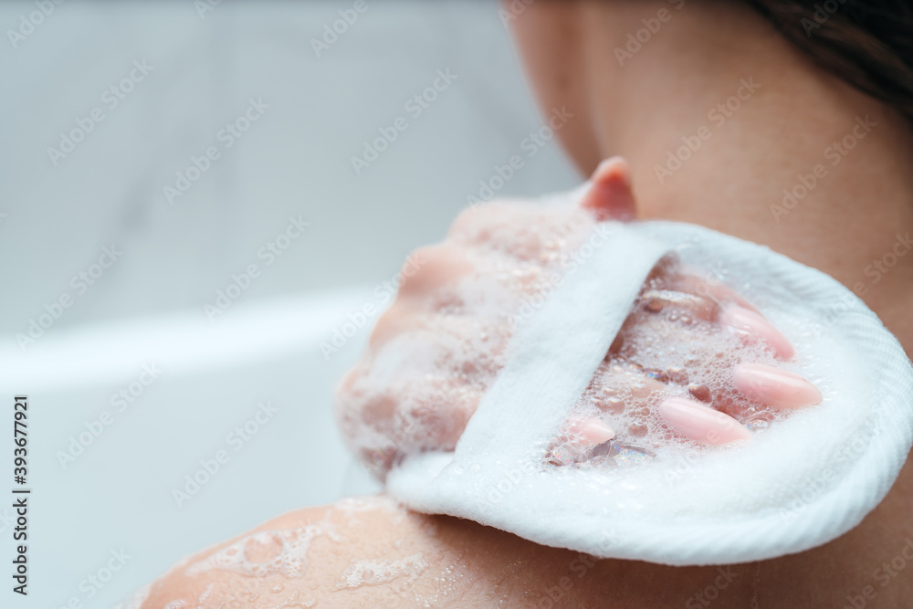 Fototapeta premium Woman's shoulder close-up. The girl lathers her shoulder with a washcloth, sits in the bath. Skin and body care. Relaxation. asparagus procedures