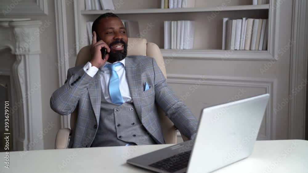 handsome black man is resting in armchair in his office and talking cheerfully by cell phone handsome black man is resting in armchair in his office and talking cheerfully by cell phone