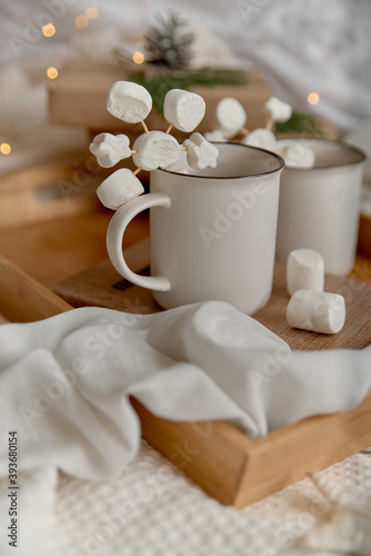Hot cocoa with marshmallow in a white ceramic mug,  on a wooden tray and wrapped boxes. The concept of cosy holidays and New Year. Selective focus