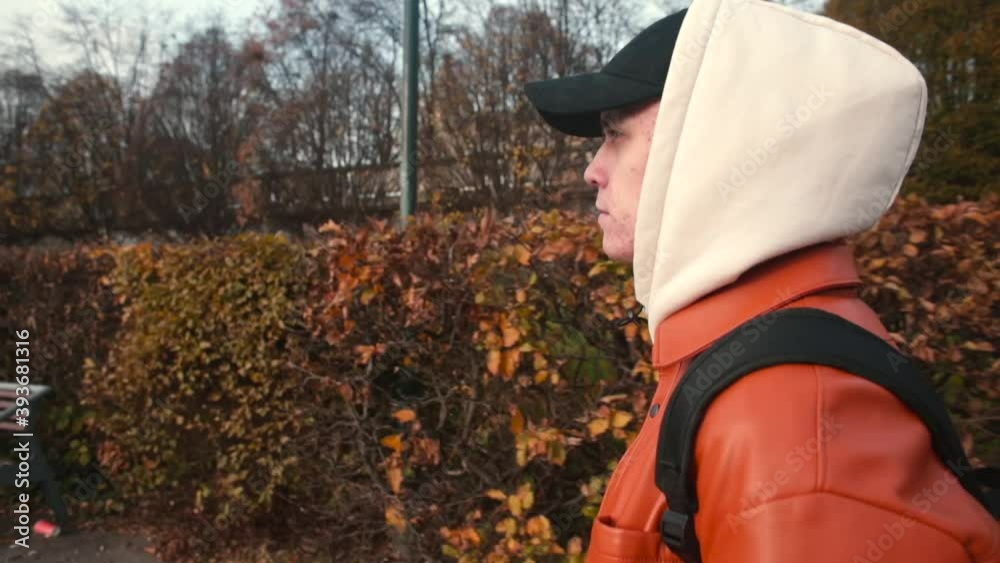 A guy in a cap and a hood on his head moves through the city park. Walking around the city. Using a backpack to carry things. Camera movement. A guy in a cap and a hood on his head moves through the city park. Walking around the city. Using a backpack to carry things. Camera movement.