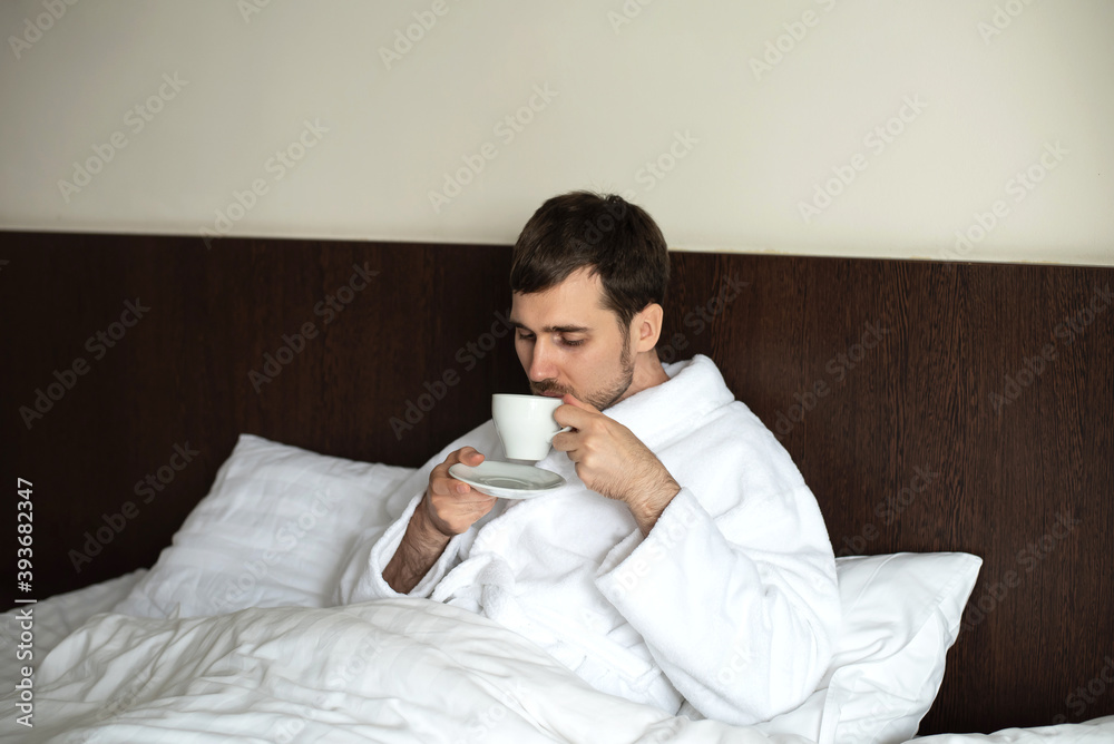 A young man in a white Terry-cloth robe in bed. A young man in a white Terry-cloth robe in bed.