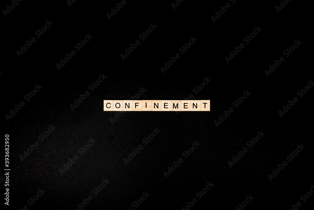Wooden letters on a black background forming the word “confinement”. Second wave during Coronavirus pandemic concept.