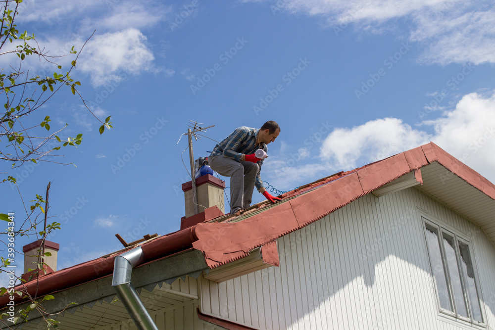 man with a compressor paints the roof,spraying spray paint on the roof of the roofer builder
