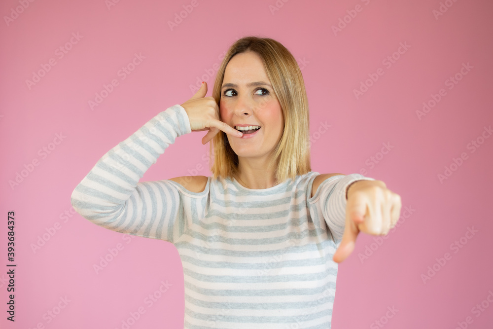 Cheerful blond woman smiling is gesturing to call her with a hand. She is wearing casual t-shirt and stands on a pink background Cheerful blond woman smiling is gesturing to call her with a hand. She is wearing casual t-shirt and stands on a pink background