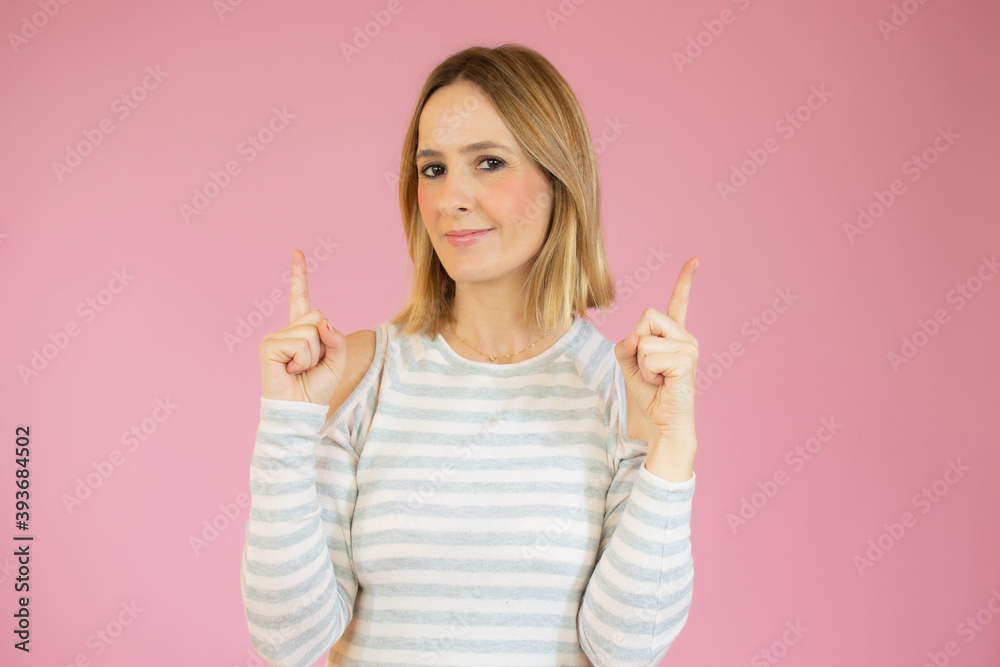 Portrait of a happy young woman dressed in casual t-shirt pointing fingers up at copy space isolated over pink background Portrait of a happy young woman dressed in casual t-shirt pointing fingers up at copy space isolated over pink background