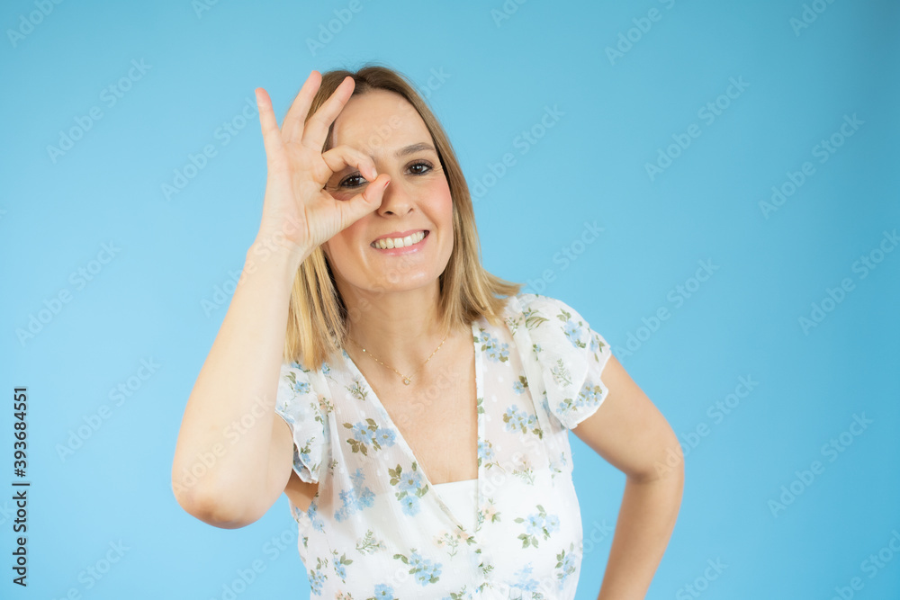 Young woman wearing casual t-shirt standing over blue isolated background smiling, eye looking through fingers with happy face. Young woman wearing casual t-shirt standing over blue isolated background smiling, eye looking through fingers with happy face.