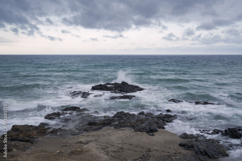 Seascape on a cloudy day with strong waves breaking against the rocks.