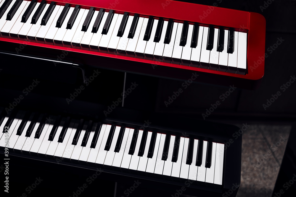 Fototapeta premium Electronic synthesizers (piano keyboards) close-up shot with dark background. Beautiful red and black musical keyboards with balck and white keys. Modern, minimalistic look, top view.