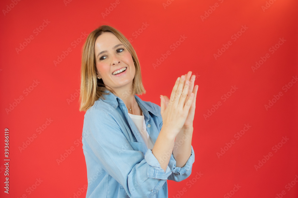 Young pretty woman feeling happy and successful, smiling and clapping hands, saying congratulations with an applause against red wall Young pretty woman feeling happy and successful, smiling and clapping hands, saying congratulations with an applause against red wall