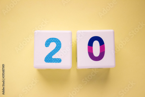 Close-up photo of a white plastic cubes with a colorful number 20 on a yellow background. Object in the center of the photo