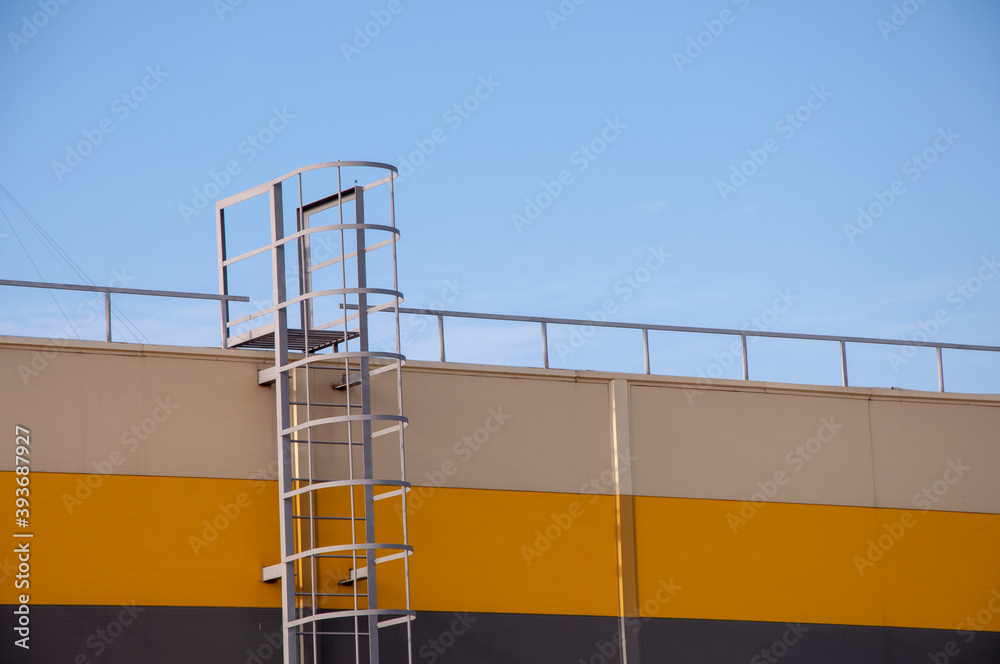 Modern beige, yellow and dark grey house with metal staircase on the blue sky background. Modern beige, yellow and dark grey house with metal staircase on the blue sky background.