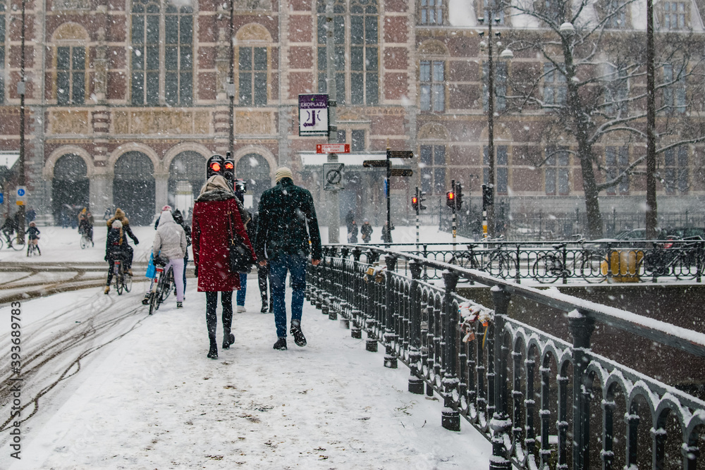 Obraz premium Couple walking under the snow next to a bridge in the city.