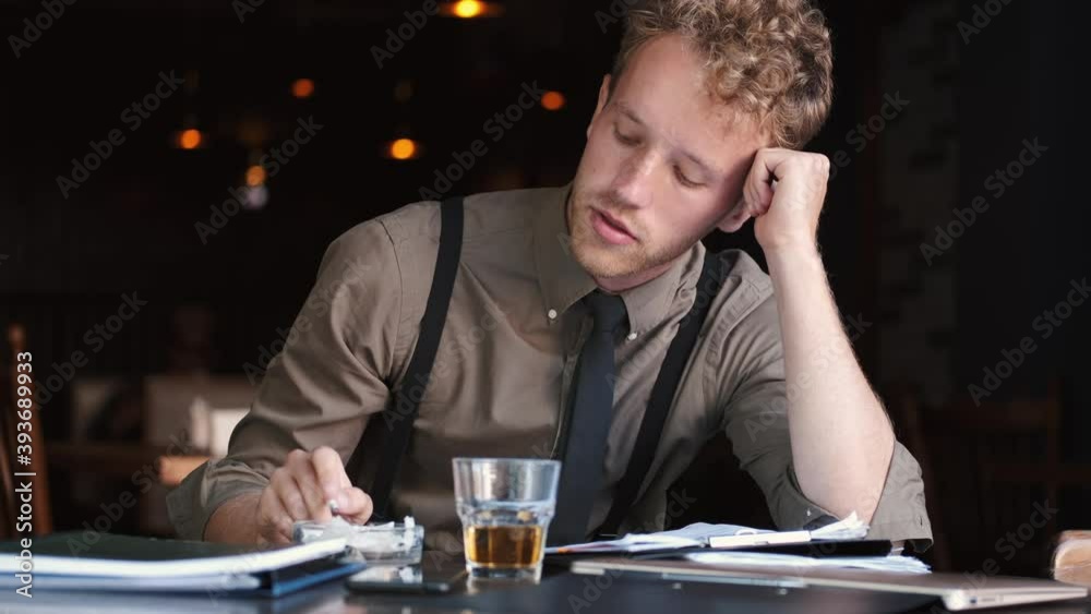 A businessman in suit is working in a cafe. The stylish man is drinkingwhiskey and reading a notebook. A businessman in suit is working in a cafe. The stylish man is drinkingwhiskey and reading a notebook.