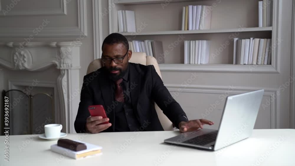 busy businessman is working in his office, black man is sitting at table with laptop and checking message in smartphone busy businessman is working in his office, black man is sitting at table with laptop and checking message in smartphone