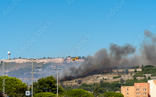 fire starts on the hills of Marseille, near Marignane airport. yellow fire-fighting plane is going to throwing water on it.  photo