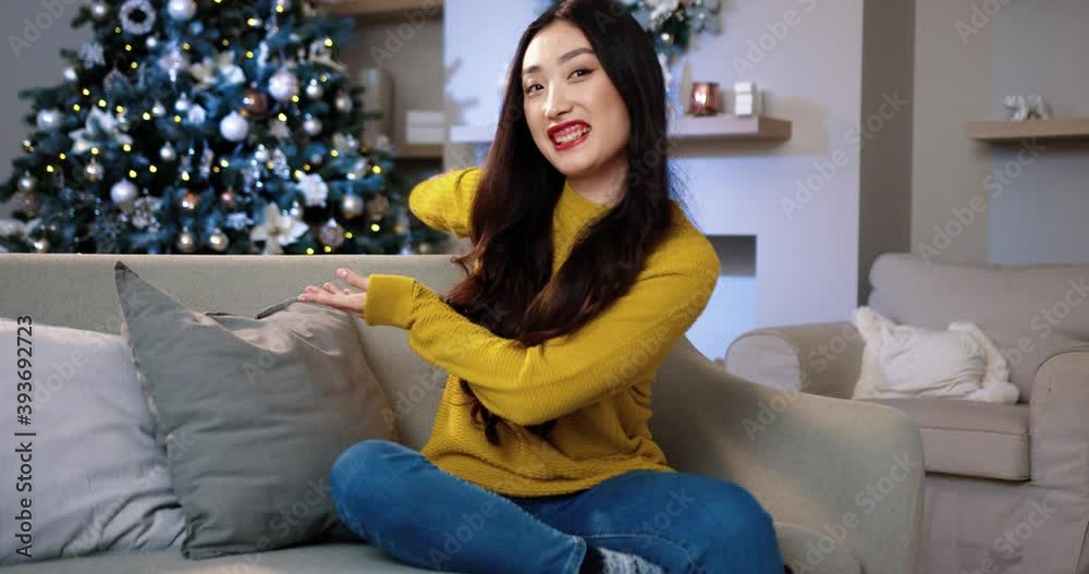 Portrait of Asian cheerful young beautiful woman in cozy room showing her decorated glowing christmas tree while talking recording video blog wishing happy holidays on New Year's Eve. Blogging concept Portrait of Asian cheerful young beautiful woman in cozy room showing her decorated glowing christmas tree while talking recording video blog wishing happy holidays on New Year's Eve. Blogging concept