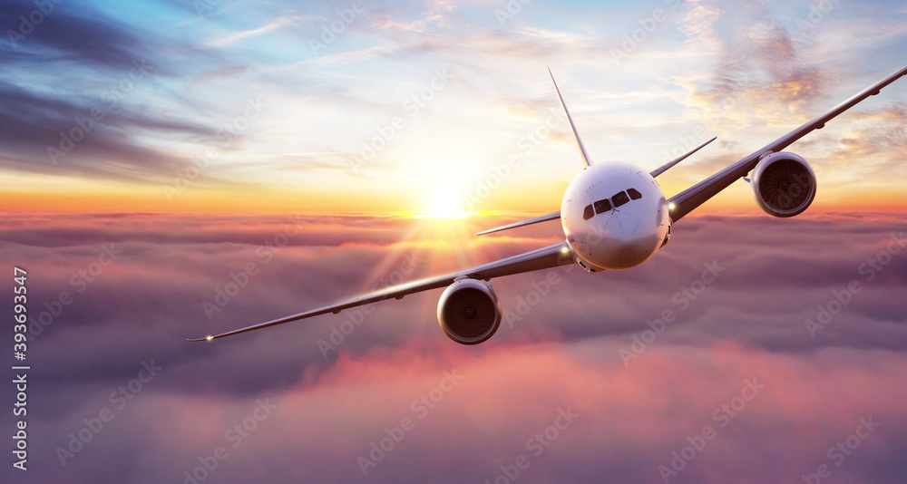 Fototapeta Commercial airplane flying above clouds in dramatic sunset light.