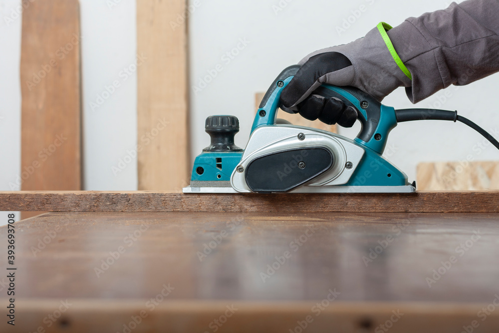 Carpenter working with electric planer on wood lath on desk, on background oriented strand board Carpenter working with electric planer on wood lath on desk, on background oriented strand board