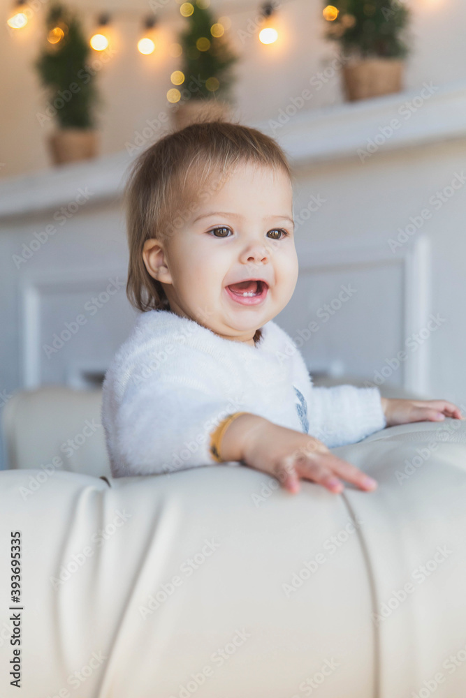 Baby on sofa near christmas tree is smiles so that two teeth are visible Baby on sofa near christmas tree is smiles so that two teeth are visible