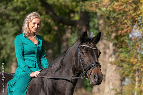 Portrait of a blonde girl in a vintage green dress with a big skirt posing with a brown horse. Selective focus © Dasya - Dasya