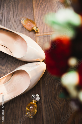 Pair of elegant and stylish bridal shoes with wedding rings and a bouquet of roses and other flowers
