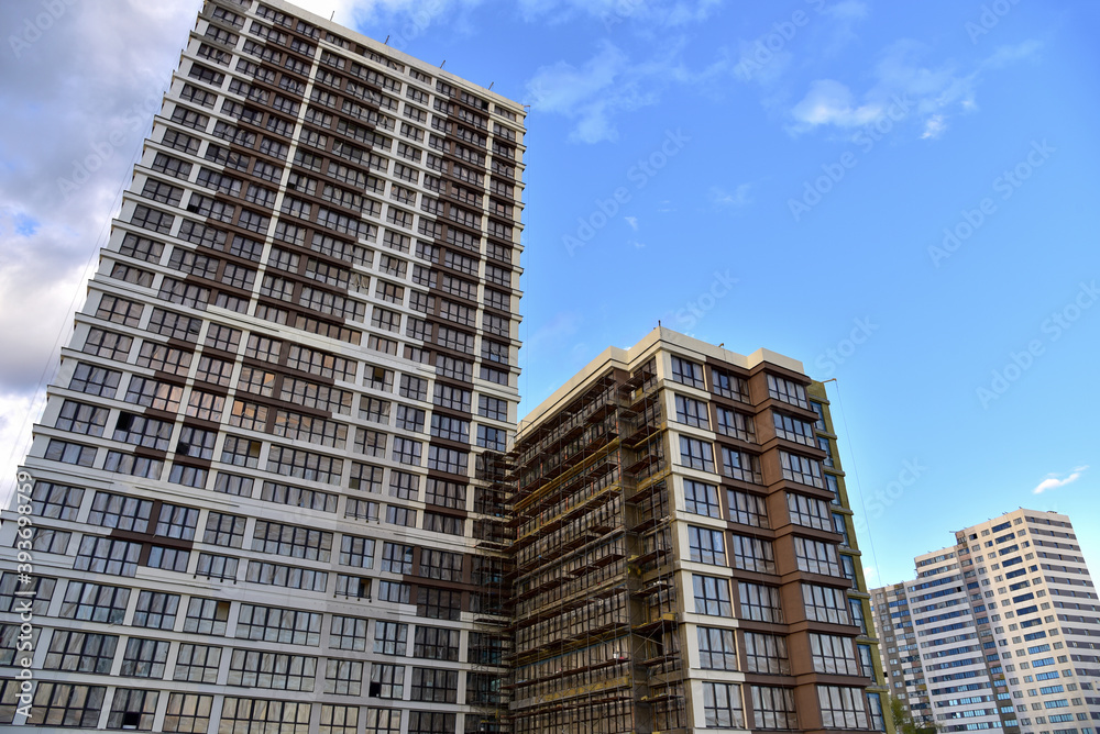 Scaffolding used in construction new building. Facade of a new modern high-rise residential building. Skyscraper on blue sky background. Tall house renovation project, government programs. Scaffolding used in construction new building. Facade of a new modern high-rise residential building. Skyscraper on blue sky background. Tall house renovation project, government programs.