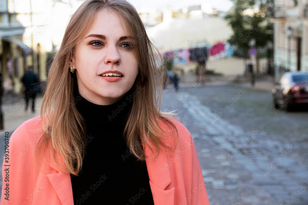 Portrait of a young woman in a bright pink jacket walking down the street on a warm autumn day